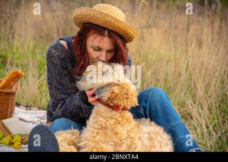 Ritratto di una donna di 40 anni in un cappello di paglia con un cane in un picnic. Foto Stock