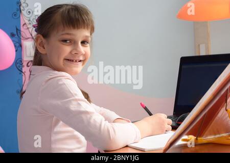 Ragazza in buona spirit che fa i compiti alla scrivania a casa Foto Stock