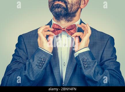 Felice uomo barbuto con abito scuro, camicia blu, cravatta farfalla rossa di regolazione isolato su sfondo verde giallo gradiente. Direttore sorridente ed elegante. Foto Stock