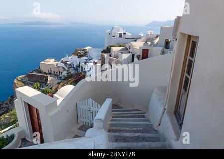 Scala giù alle tradizionali case greche bianche lungo la costa con l'oceano blu a Oia, Santorini, Grecia Foto Stock