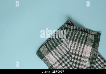 Sfondo turchese chiaro con un asciugamano verde a scacchi. Asciugamano da cucina piegato casualmente. Background minimalistico multitasking. Vista dall'alto. Foto Stock