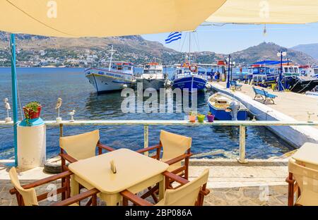 Taverna fronte mare che si affaccia sulle barche da pesca lungo il mare della piccola città portuale di Telendos Island, Kalymnos, Dodecanese, Grecia Foto Stock