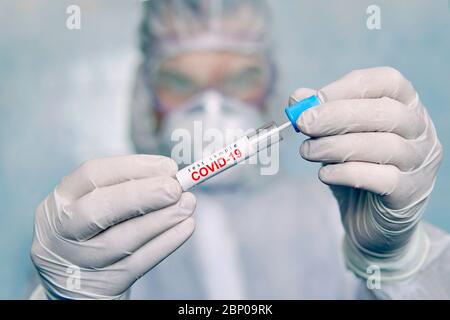 un uomo in tuta di protezione chimica contiene una provetta per l'analisi. COVID-19. Campione di tampone coronavirus COVID-19. Tampone test coronavirus. Trasporto usato Foto Stock