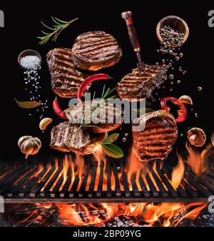 Bistecche di manzo e verdure alla griglia in movimento che cadono sulla griglia aperta. Foto concettuale del processo di cottura della carne o del barbecue. Foto Stock