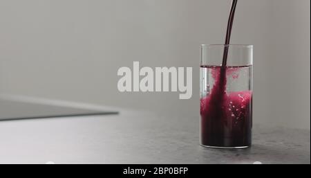 il succo di mirtillo versare nell'acqua in un bicchiere di highball in cucina piano di lavoro Foto Stock