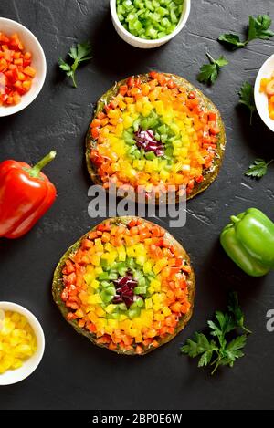 Arcobaleno veggie peperoni pizza campana su fondo di pietra nera. Vegetariano vegano o concetto di cibo sano. Piatto dietetico senza glutine. Vista dall'alto, disposizione piatta Foto Stock