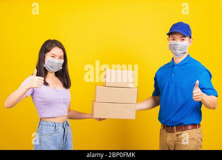 Asian bella donna e bell'uomo che indossa la maschera facciale di protezione contro il coronavirus, accettando scatole di consegna, studio girato isolato sul retro giallo Foto Stock
