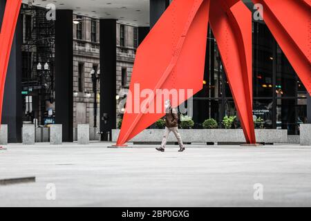 Un uomo con una maschera facciale cammina vicino alla scultura di Flamingo rosso brillante creata dall'artista americano Alexander Calder, che si trova a Chicago. Foto Stock