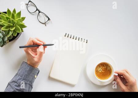 Uomo che lavora scrivendo nel blocco note e bevendo caffè Foto Stock