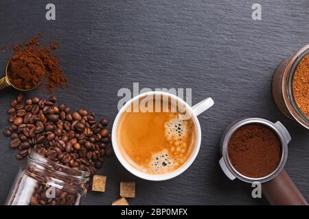 Vista dall'alto di una tazza di espresso, caffè in grani, macinato e zucchero su un tavolo in pietra nera. Foto Stock