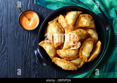 Empanadas di pollo di bufala piccante con un tuffo a basso contenuto calorico in una padella nera in ceramica su un tavolo di legno, vista orizzontale dall'alto, piatto, spazio libero Foto Stock