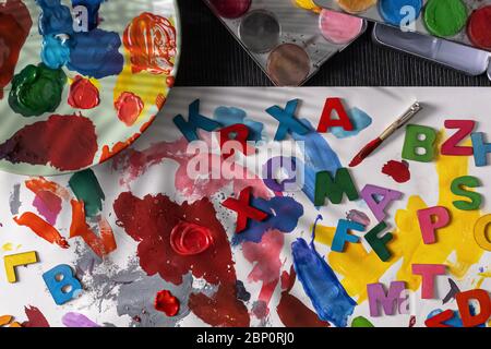 Una tabella disordinata con diversi tipi di vernici. Acquerello, oli vernici che lavorano su lettere colorate Foto Stock