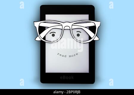 Un e-book nero con bicchieri di carta e un volto felice dove è scritto 'leggere di più' su uno sfondo blu Foto Stock