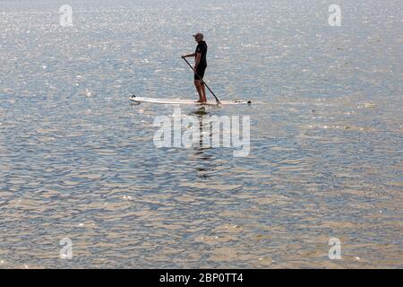 Poole, Dorset UK. 17 maggio 2020. Meteo per il Regno Unito: Calde e soleggiate alle spiagge di Poole, mentre i beachgoers si dirigono verso il mare per godersi il sole il primo fine settimana dopo i cambiamenti per alleviare le restrizioni di Coronavirus che le persone possono sedersi o prendere il sole sulla spiaggia quanto desiderano, purché aderiscano alle distanze sociali. Paddleboarder su un mare scintillante. Credit: Carolyn Jenkins/Alamy Live News Foto Stock