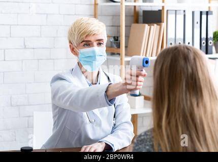 Esame del paziente. Donna medico in maschera protettiva misura la temperatura Foto Stock