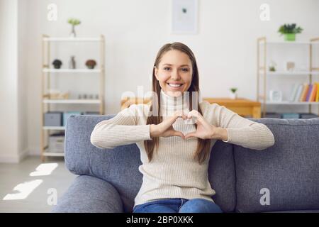 Chiamata video chat online datazione. Sorridente donna guarda la fotocamera online tiene le mani a forma di cuore in una data in una video chat su una datazione Foto Stock