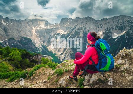 Allegra donna escursionista con zaino colorato. Donna escursionista di libertà seduto e godendo la vista con la vetta del monte Jalovec, dalla Spica Slemenova hi Foto Stock