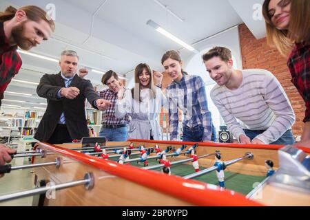 Uomini d'affari che hanno molto tempo insieme, colleghi che giocano a calcio da tavolo in un ufficio moderno Foto Stock