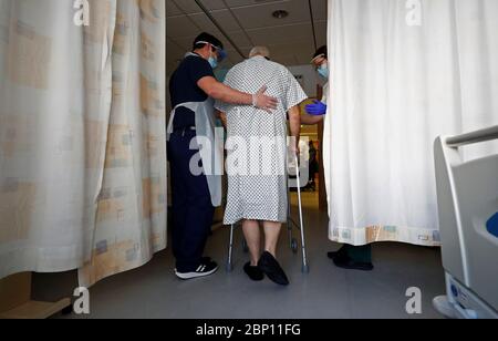 I terapisti professionali Jason Smith (a sinistra) e Grace Rowan (a destra) assistono il paziente del coronavirus Peter Dunn (centro) nel camminare ancora dopo aver lasciato le cure intensive al Royal Blackburn Teaching Hospital a East Lancashire durante lo scoppio della malattia del coronavirus. Foto Stock