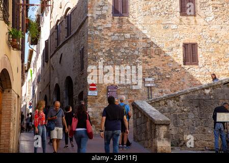 San Gimignano città medievale collinare in Toscana, turisti e visitatori camminano all'interno delle mura cittadine e curiosano nell'architettura locale dell'Italia soleggiata Foto Stock