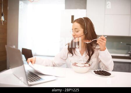 Donna lavora da casa. Un dipendente si trova in cucina e ha molto lavoro su laptop e tablet, oltre a videoconferenze e riunioni. Utilizza le cuffie Foto Stock