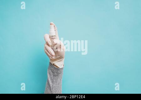 Mano della donna in guanto medico protettivo mano che tiene flacone di spruzzatura dell'igienizzatore su sfondo blu Foto Stock