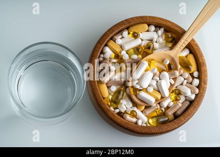 Vista dall'alto di pillole, compresse e farmaci diversi in una ciotola di legno con cucchiaio e bicchiere d'acqua. Foto Stock