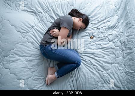 Donna sdraiata sul letto vicino a un mucchio di pillole sopra la vista Foto Stock