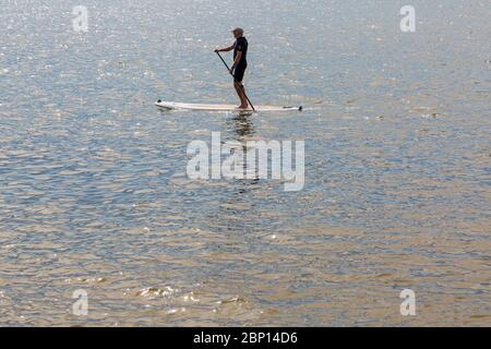 Poole, Dorset UK. 17 maggio 2020. Meteo per il Regno Unito: Calde e soleggiate alle spiagge di Poole, mentre i beachgoers si dirigono verso il mare per godersi il sole il primo fine settimana dopo i cambiamenti per alleviare le restrizioni di Coronavirus che le persone possono sedersi o prendere il sole sulla spiaggia quanto desiderano, purché aderiscano alle distanze sociali. Paddleboarder sul mare scintillante. Credit: Carolyn Jenkins/Alamy Live News Foto Stock