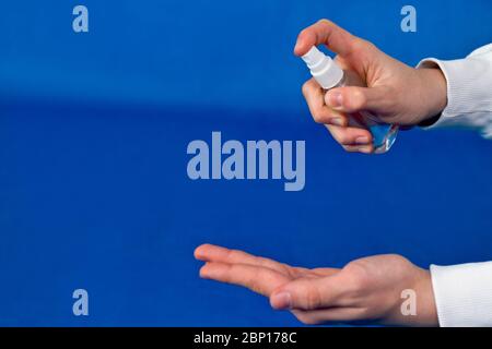 Mani umane usare spray, disinfettante, antisettico in bolla, vaso su sfondo blu. Foto Stock