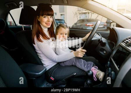 Donna caucasica piuttosto giovane, madre con una bambina sono seduti davanti al sedile mentre il veicolo si è fermato. Madre e bambino sorridenti Foto Stock