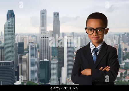 infanzia e gente concetto-piccolo afroamericano ragazzo con occhiali in abito da lavoro su sfondo città. Posa del sorriso sicuro e fresco. Foto Stock