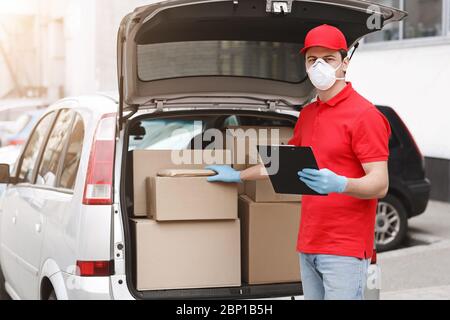 Il consegnatore sta controllando il pacco. Corriere con tablet, mettere la mano sulla scatola in auto Foto Stock