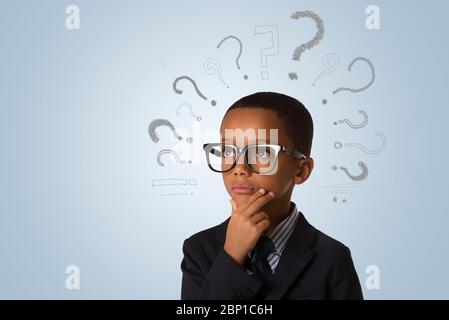 Bel ragazzo afro-americano che indossa occhiali e pensa con molti punti interrogativi su sfondo blu. Concetto di idee, confusione e solut Foto Stock