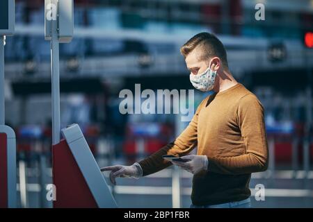Uomo che indossa la maschera e usa il dispositivo di check-in all'aeroporto. Temi che viaggiano durante la pandemia e la protezione personale. Foto Stock