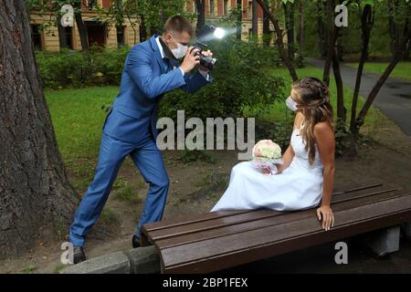 Fotografando sposo e sposa nel parco, indossano maschere di protezione facciale durante l'infezione da coronavirus covid-19 pandemic, stagione di nozze estate Foto Stock