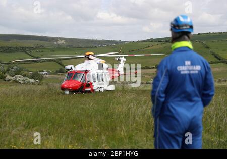 Un membro della squadra di ricerca e salvataggio della guardia costiera di HM guarda sopra come un elicottero AgustaWestland AW189 da HM Coastguard atterra sul lato della scogliera vicino a Overcombe in Dorset, durante un esercizio di addestramento. Foto Stock