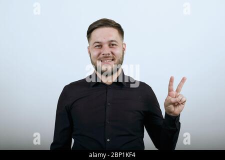 Happy Male sorride, mostra due dita come un segno di Pace. Foto Stock