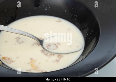 Un po' di latte e cornflakes in un piatto nero. Primo piano basso e affamato. Foto Stock