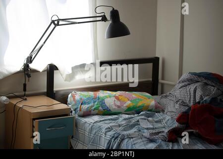Camera singola disordinata. Solo uomo. Accanto alla finestra è presente una lampada da tavolo. Foto Stock