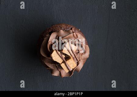 Cupcake al cioccolato con gelato alla crema di cacao, torta di tazza decorata con girls al cioccolato e blocchi di fondente isolati su sfondo nero rustico di legno Foto Stock