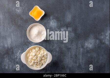 Ingredienti per preparare cheesecake fatti in casa - formaggio di cottage, farina, uova. Sfondo panetteria. Vista dall'alto Foto Stock