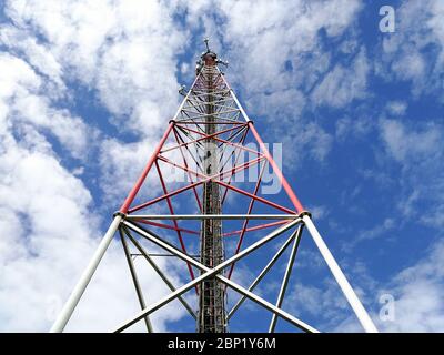 Stazione base GSM (Global System for Mobile Communication) e ripetitore torre davanti al cielo blu nuvoloso Foto Stock