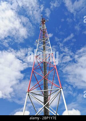 Stazione base GSM (Global System for Mobile Communication) e ripetitore torre davanti al cielo blu nuvoloso Foto Stock