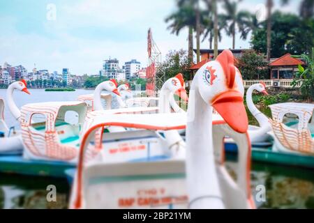 Barche a remi a forma di cigni, con edifici sfocati sullo sfondo, Hanoi, Vietnam Foto Stock