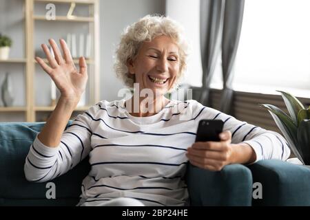 Eccitata, sorridente, nonna matura che agita la mano, tenendo una videochiamata. Foto Stock