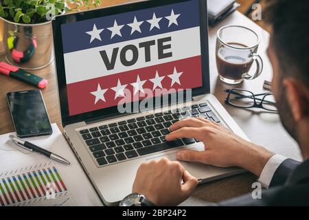 Elezioni online, votazione digitale sul concetto elettorale americano. Uomo che lavora con un computer portatile, VOTO testo sul display, sfondo ufficio. Foto Stock