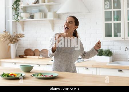 Felice giovane donna ha divertimento cantando cucina a casa Foto Stock
