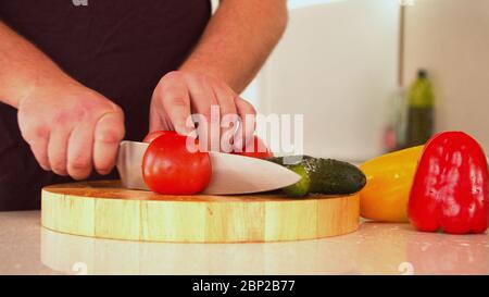 Uomo che taglia pomodori freschi rossi per insalata Foto Stock
