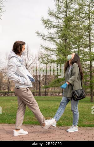Giovane coppia allegra in casualwear e maschere protettive in piedi nel parco tra alberi verdi e prati e godendo di calda giornata estiva Foto Stock